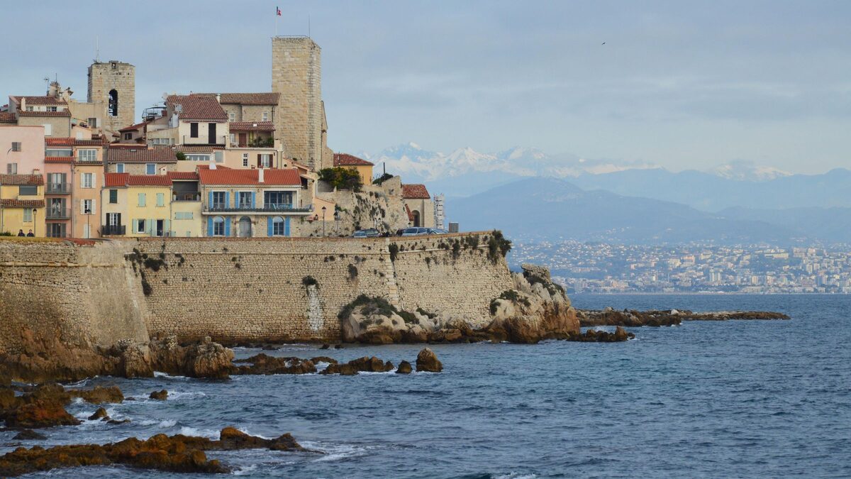 The old town of Antibes on its sea walls above the rocky shore, with the coast and mountains behind