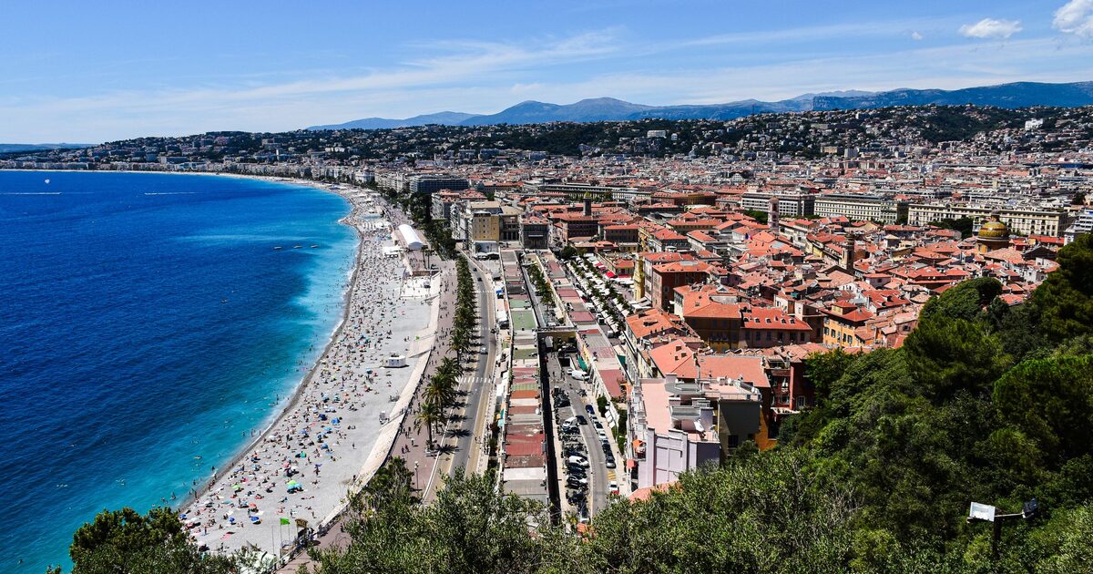 The Baie des Anges seen from Castle Hill in Nice, with the long pebble beach, the Promenade des Anglais and the red roofs of the city below green hills