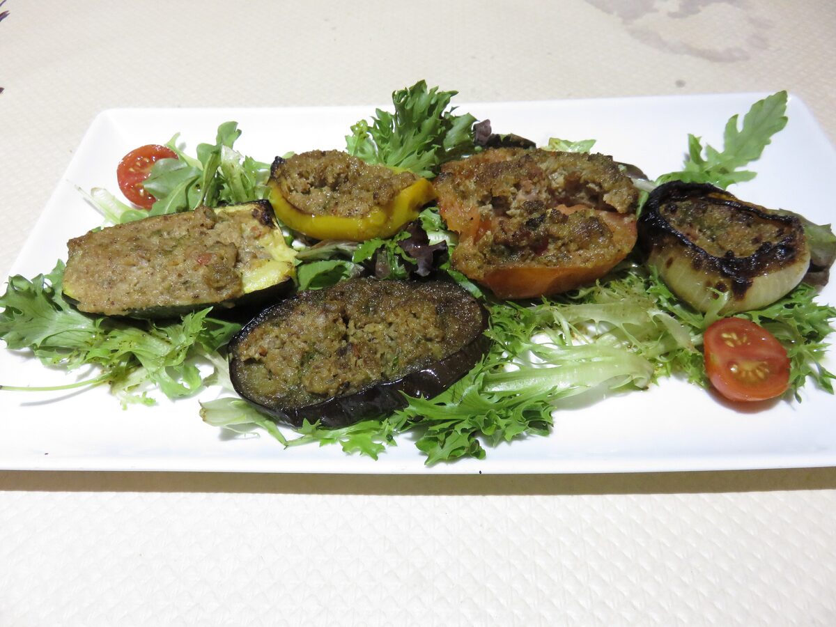 Stuffed baked tomatoes, zucchini and eggplant on a bed of rocket on a white plate