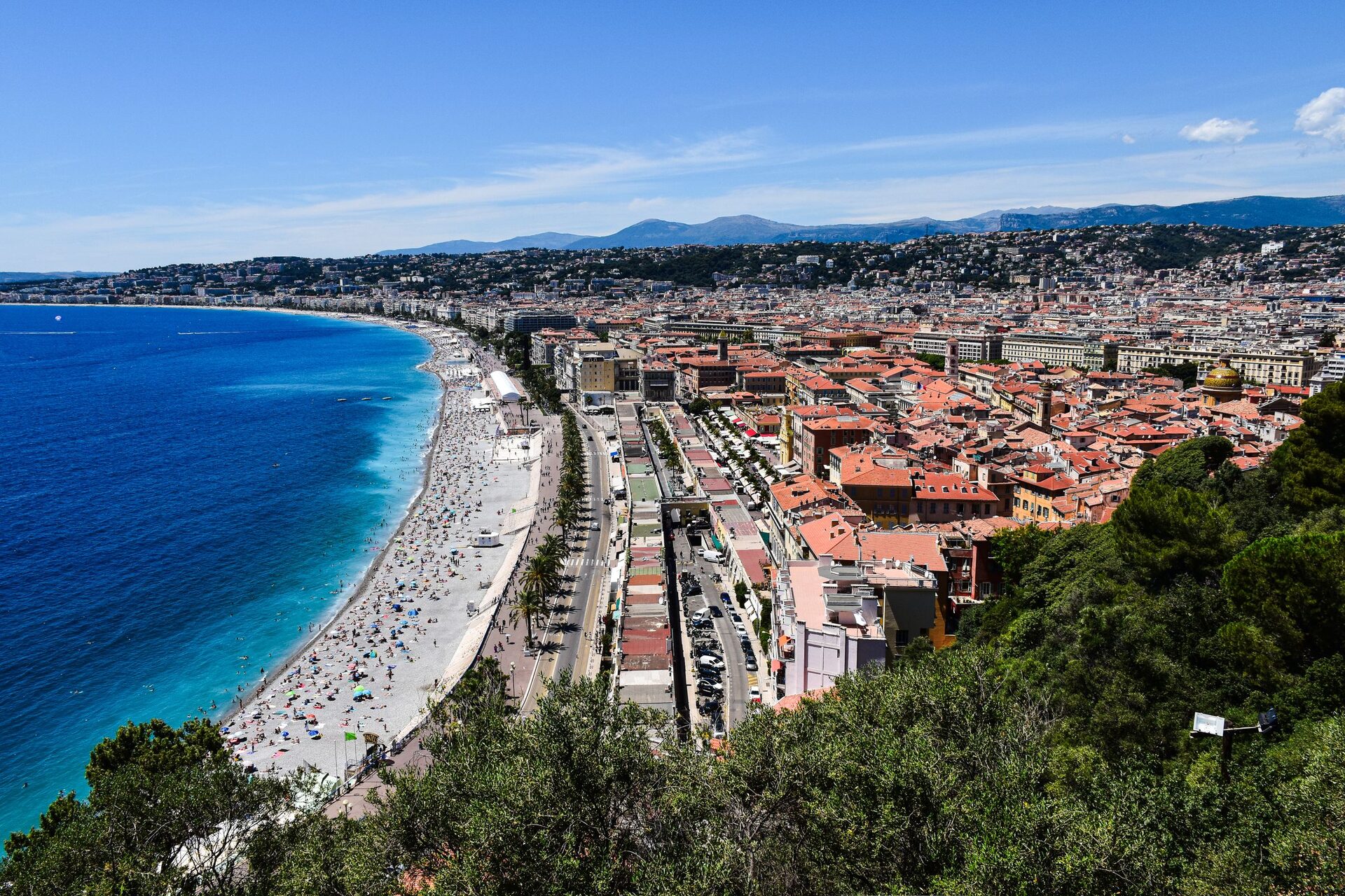 The Baie des Anges seen from Castle Hill in Nice, with the long pebble beach, the Promenade des Anglais and the red roofs of the city below green hills