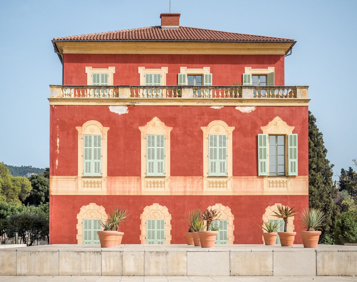 The red Genoese villa of the Musée Matisse with yellow trim, green shutters and potted plants along its front