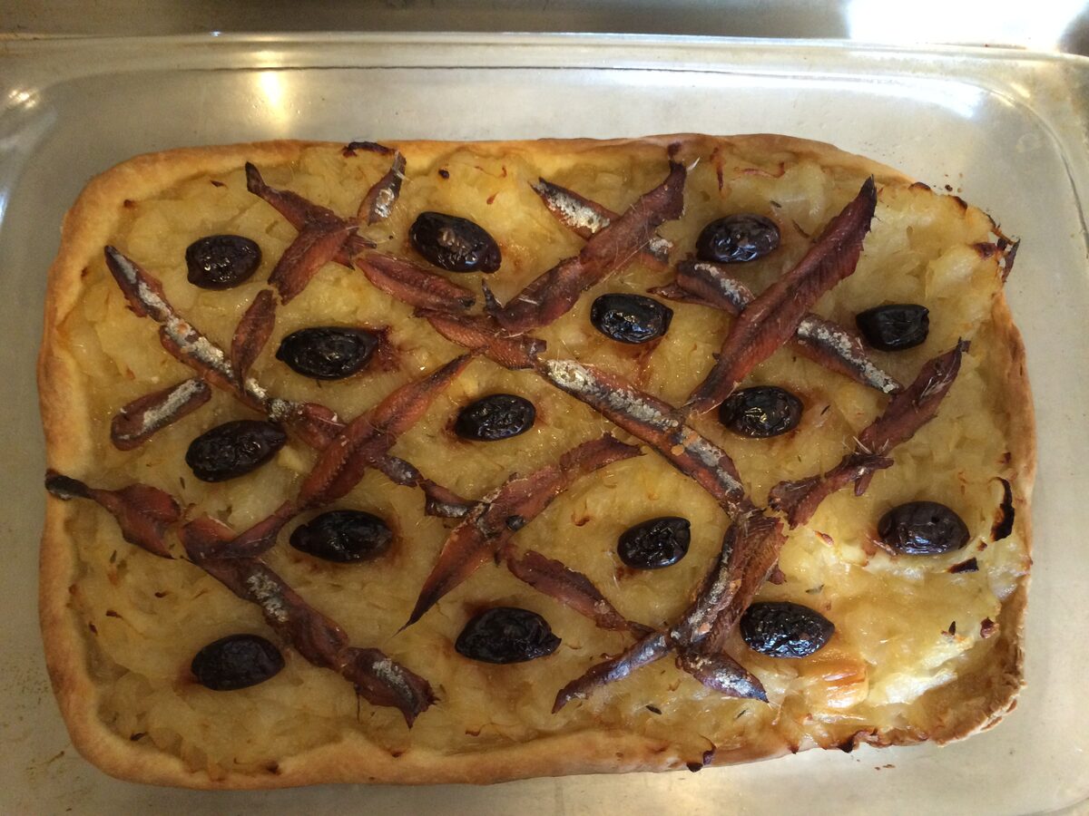 A rectangular pissaladière covered in soft onions, with a lattice of anchovies and black olives on top