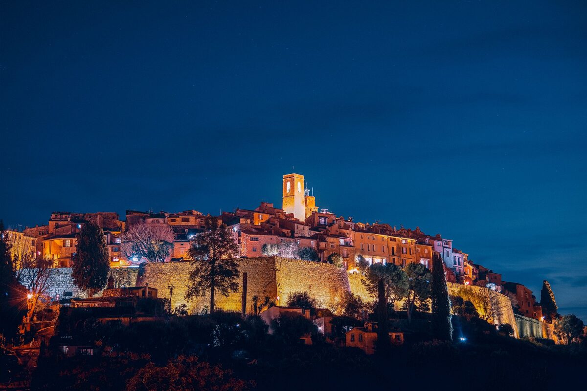 The walled hilltop village of Saint-Paul-de-Vence lit up at dusk, with its church tower against a deep blue sky