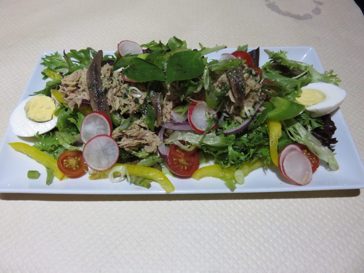 A salade niçoise on a white plate with tuna, hard-boiled egg, radishes, cherry tomatoes and peppers on leaves