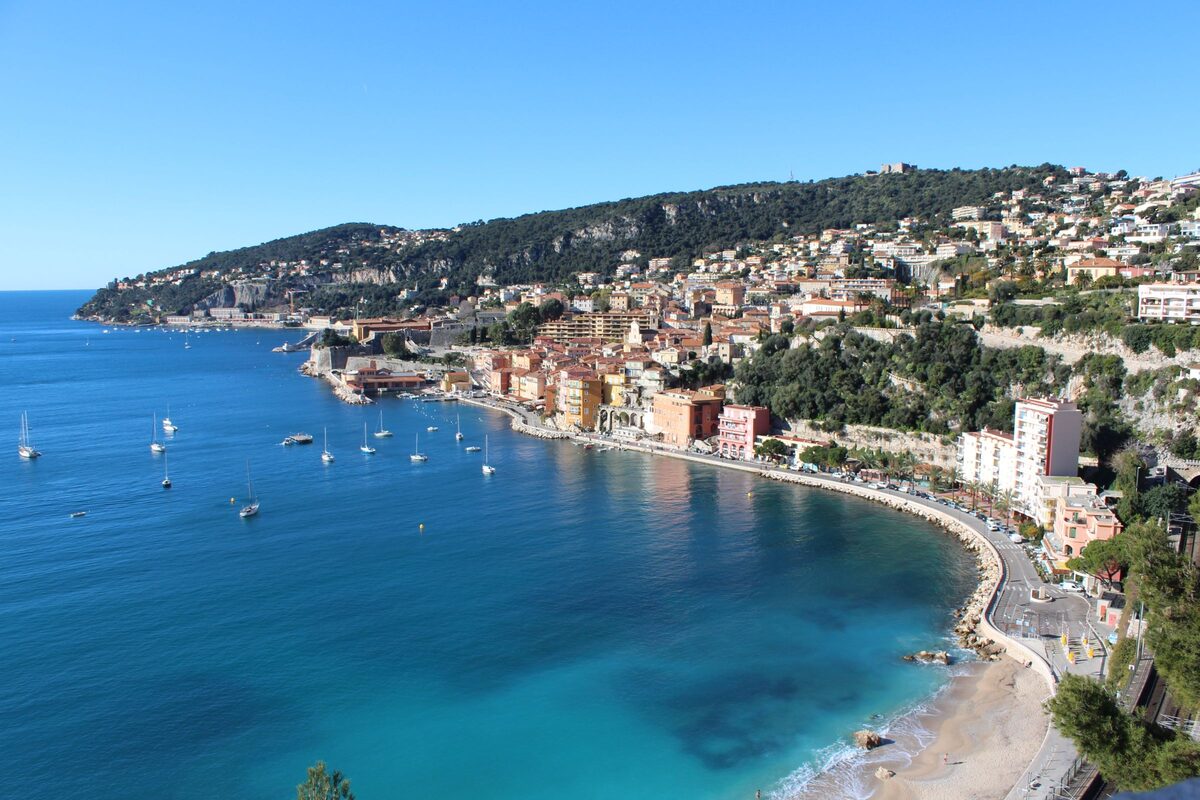 The colorful houses of Villefranche-sur-Mer along a deep blue bay full of sailboats, with green hills behind