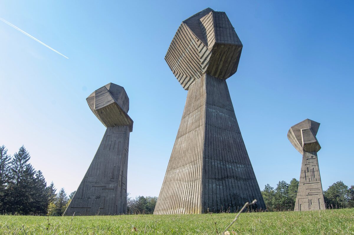 The three giant concrete fists of the Bubanj memorial rising from a grassy meadow against a clear blue sky.