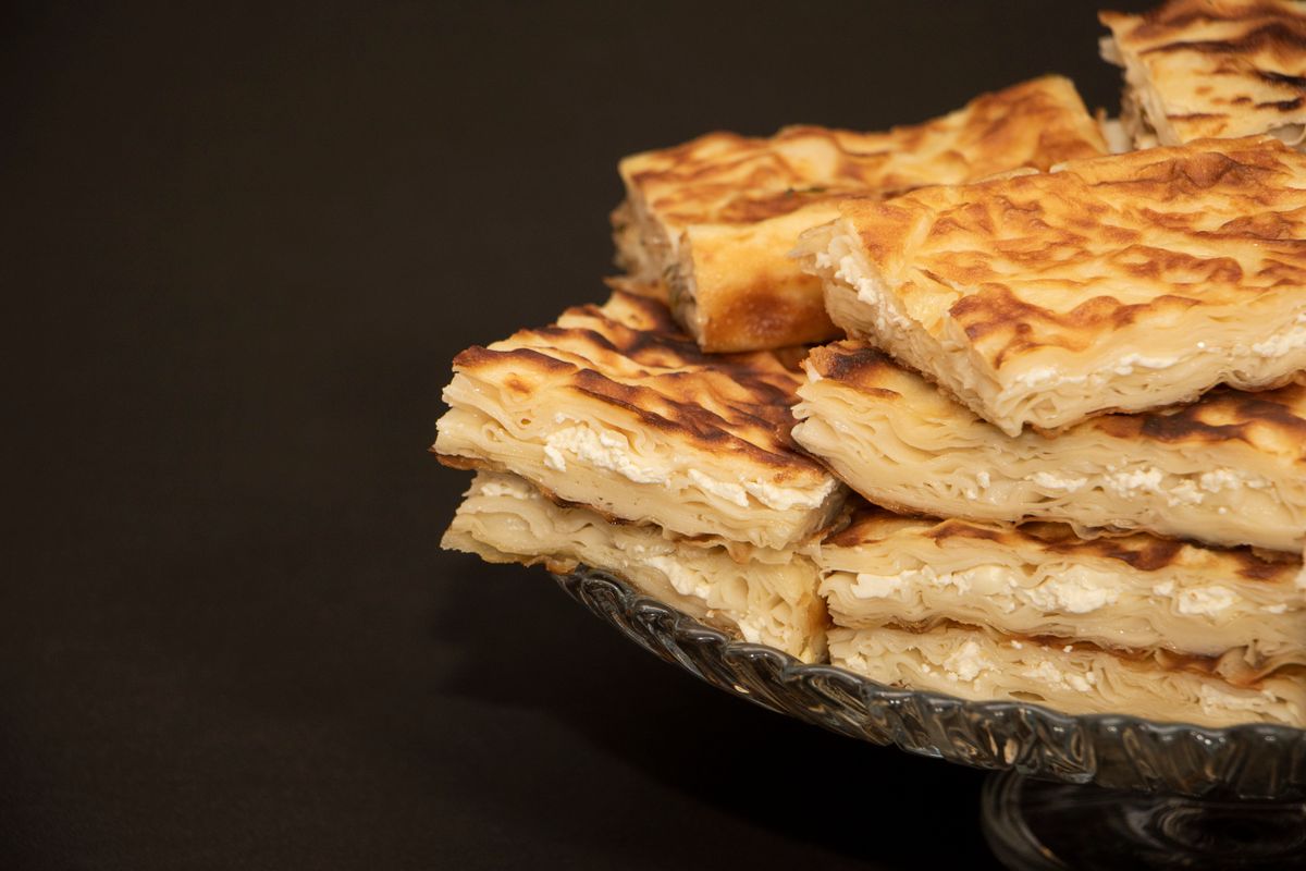 Squares of flaky cheese burek piled on a glass cake stand