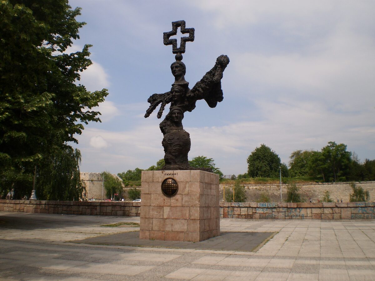 The bronze Constantine the Great monument, crowned with a cross, on a stone plinth in the paved square below the walls of Niš Fortress.