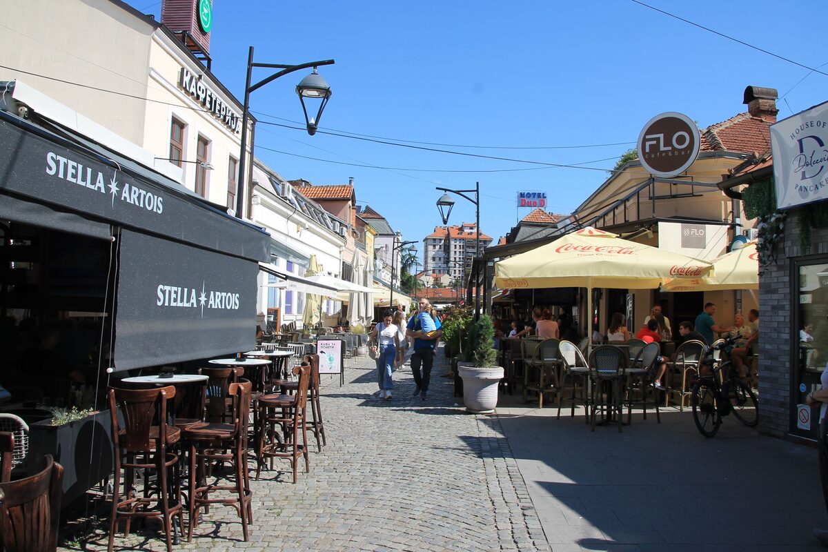 The cobbled lane of Kazandžijsko sokače on a sunny day, lined with café terraces, umbrellas and low old houses.