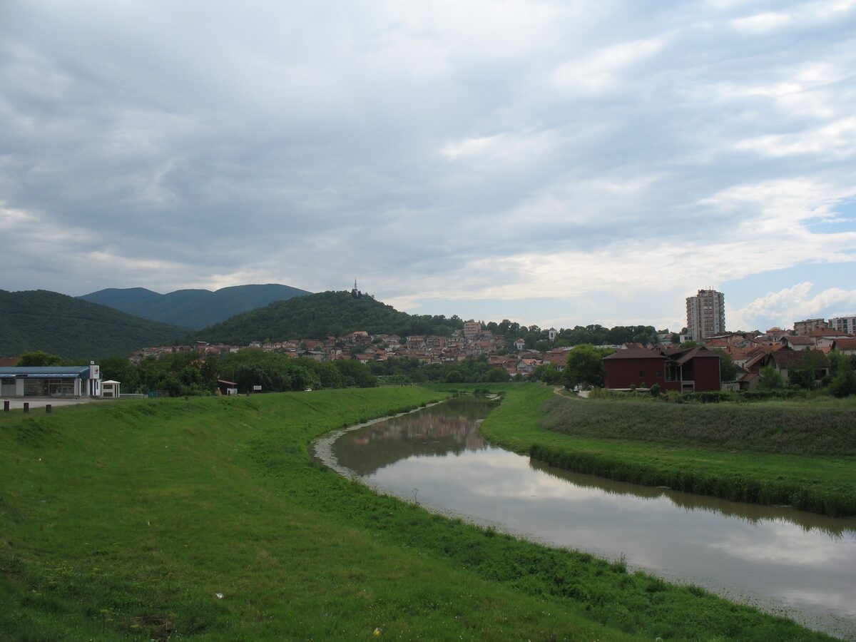 The Toplica river curving between green embankments toward Prokuplje, with the wooded Hisar hill and its tower rising above the town.