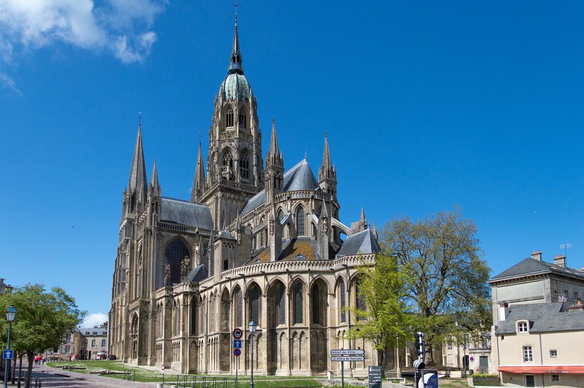 Bayeux Cathedral seen from the east, its Gothic apse and tall spires against a blue sky