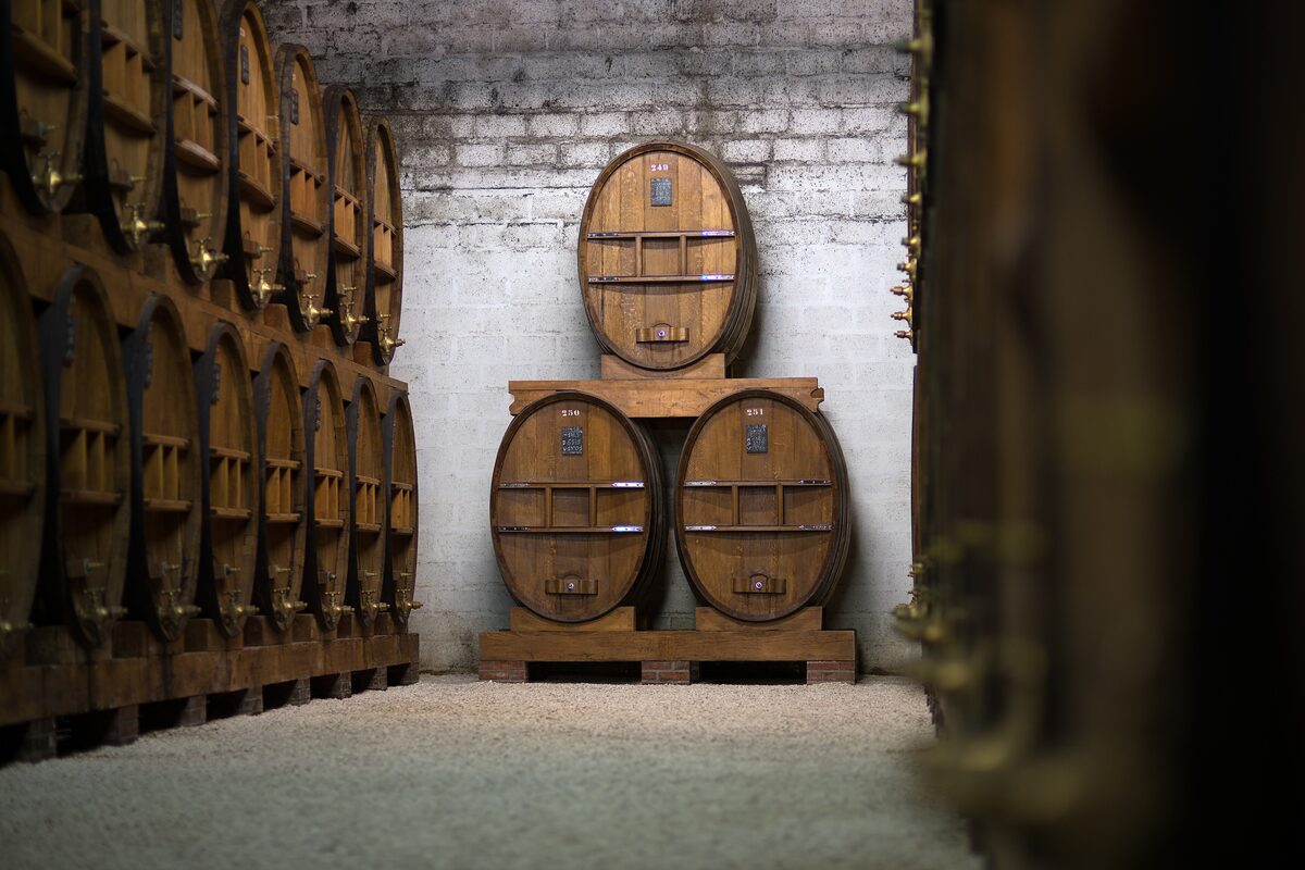 Calvados ageing in large oak casks in a dim cellar, with the numbered barrels stacked in the middle