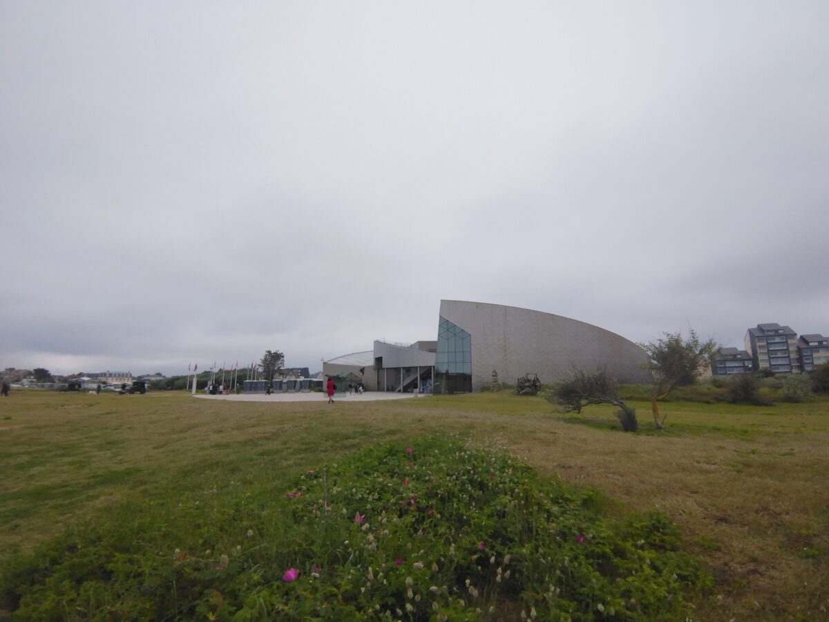 The curved grey building of the Juno Beach Centre on the grass above the coast at Courseulles-sur-Mer