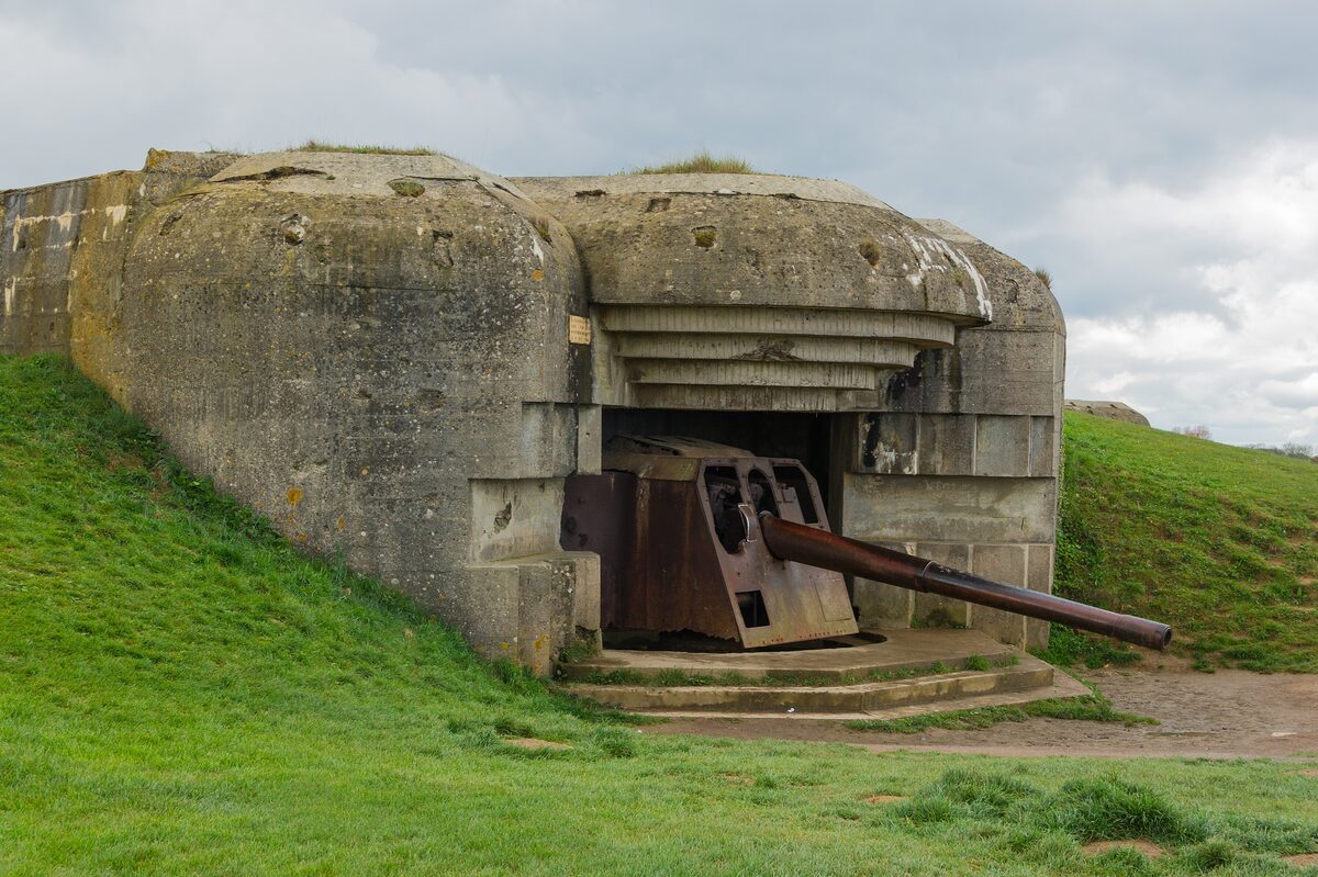 One of the heavy naval guns of the Longues-sur-Mer battery in its concrete casemate, the rusted barrel pointing out over the grass