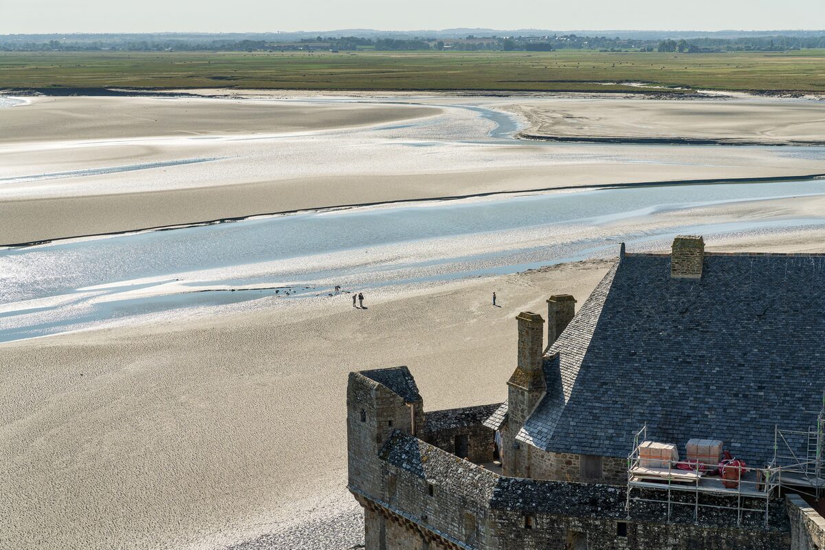 The sand flats and winding tidal channels of the bay seen from the Mont-Saint-Michel ramparts, with a slate roof in front