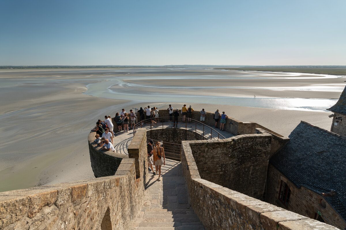 Visitors on the stone ramparts of Mont-Saint-Michel, with the tidal flats of the bay stretching out beyond the wall