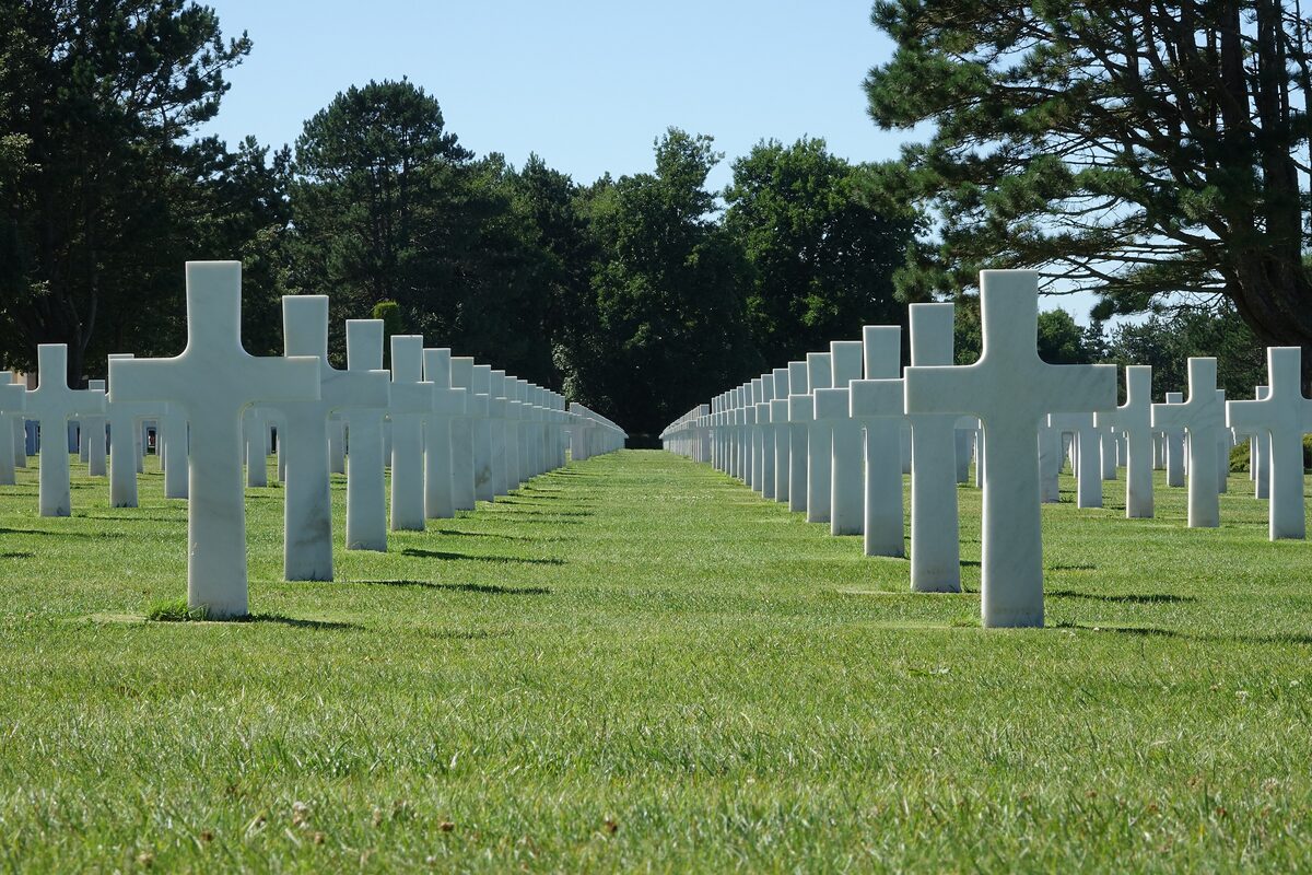 Rows of white marble crosses across the grass at the Normandy American Cemetery, under tall trees