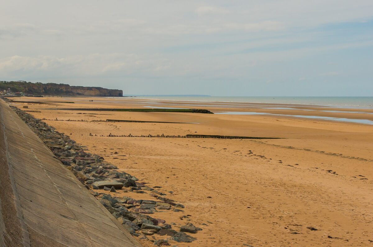 Omaha Beach at low tide: the wide sand flats, the concrete sea wall on the left and the wooden posts out to the sea
