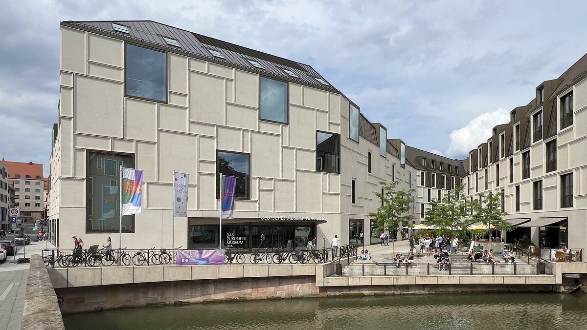 The pale stone and glass facade of the Deutsches Museum Nürnberg beside its plaza