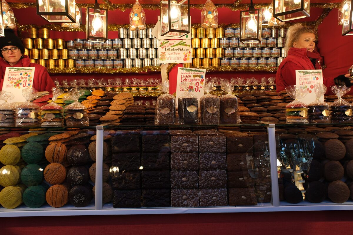 A market stall piled with Lebkuchen in tins and boxes, with two vendors in red behind the counter
