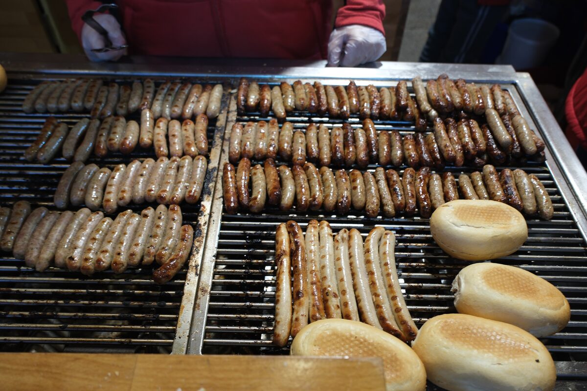 Rows of small Nuremberg bratwursts and a few bread rolls on a hot grill