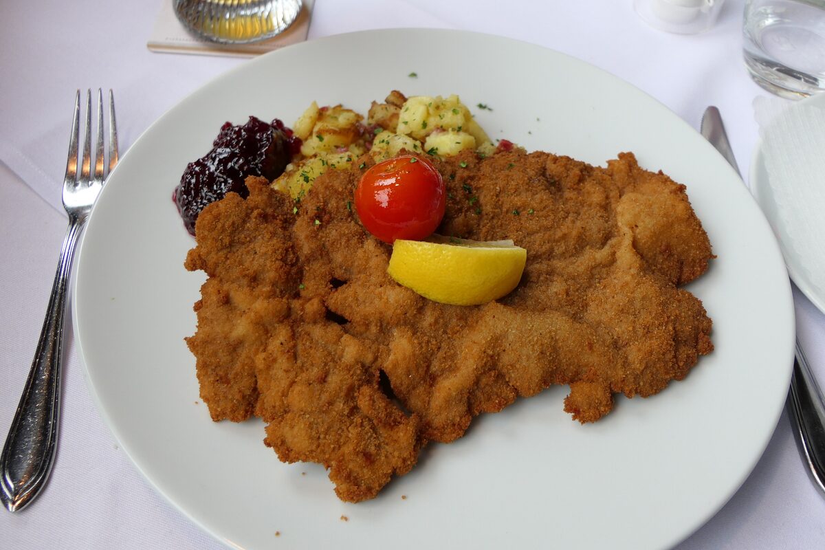 A breaded schnitzel with fried potatoes, lingonberry sauce and a lemon slice