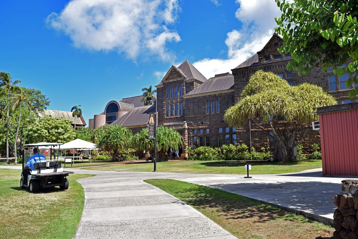 The Bishop Museum's dark stone Victorian halls and lawns under a blue sky