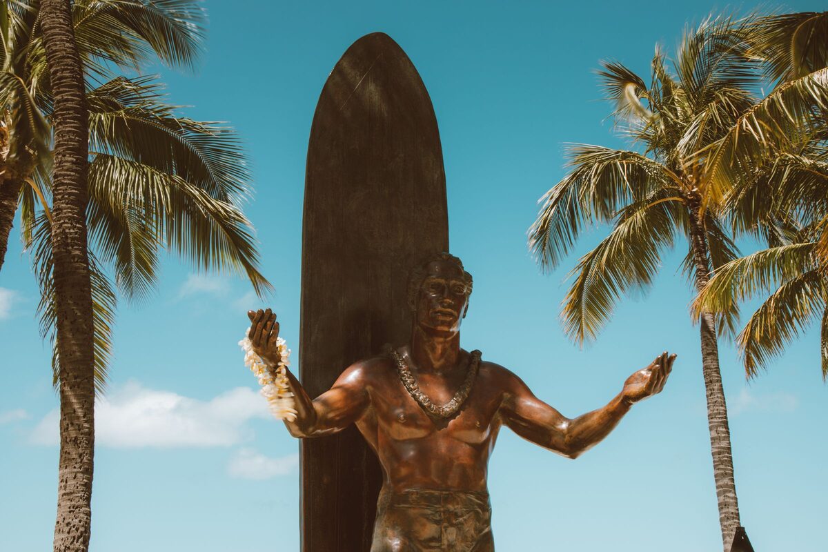 Bronze statue of Duke Kahanamoku with arms open beside a surfboard