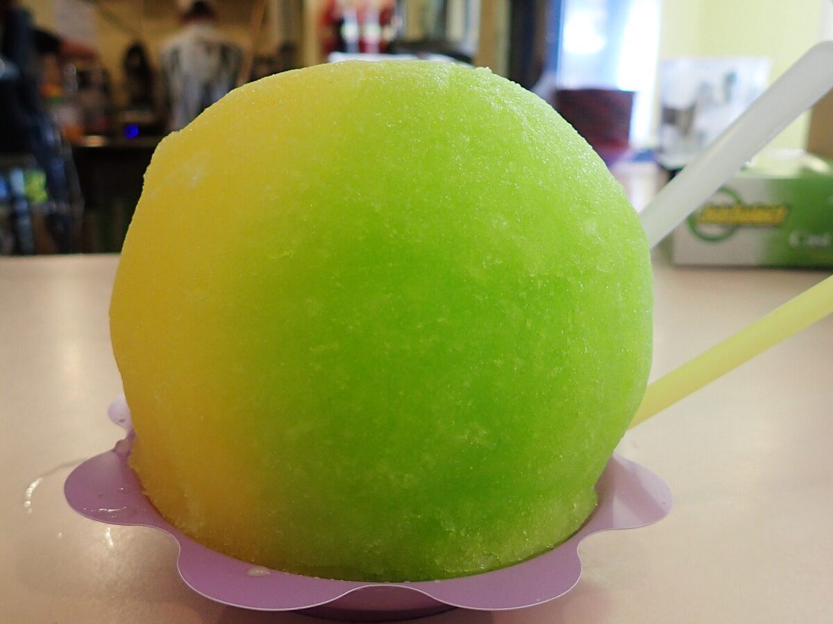 A half-yellow, half-green mound of shave ice in a purple cup
