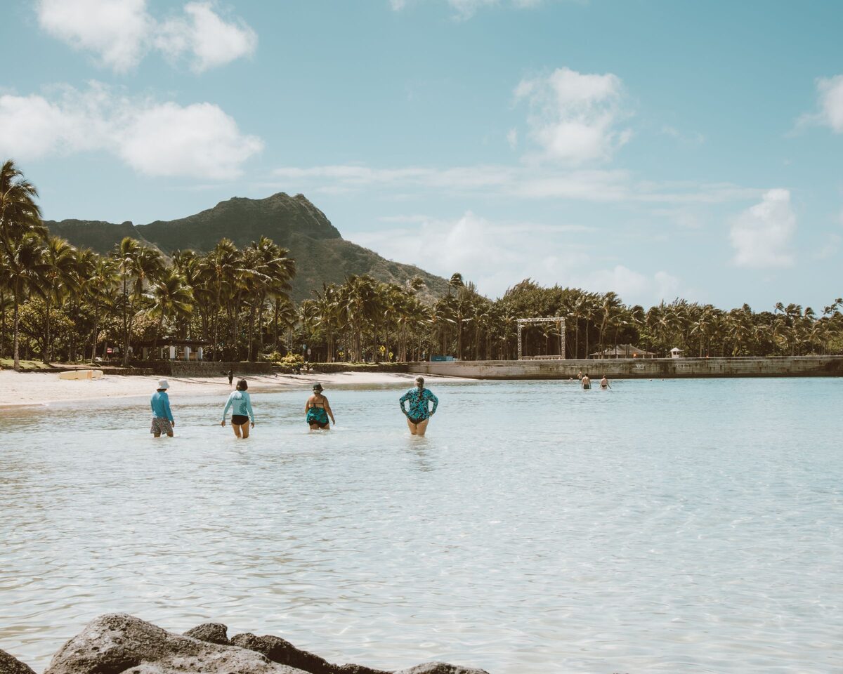Swimmers wading in the calm shallows of Kūhiō Beach with Diamond Head behind