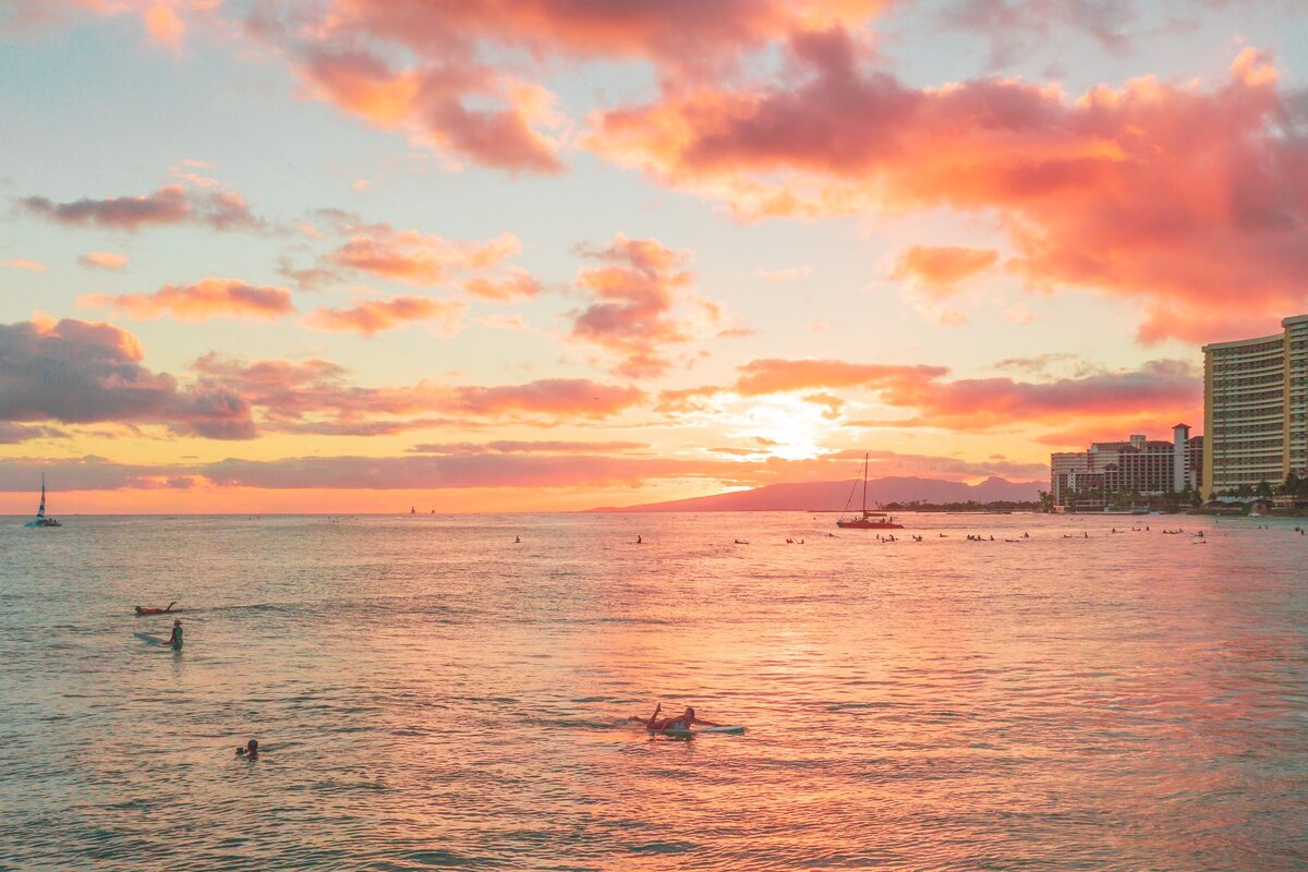 Pink sunset sky over Waikīkī with paddlers on calm water