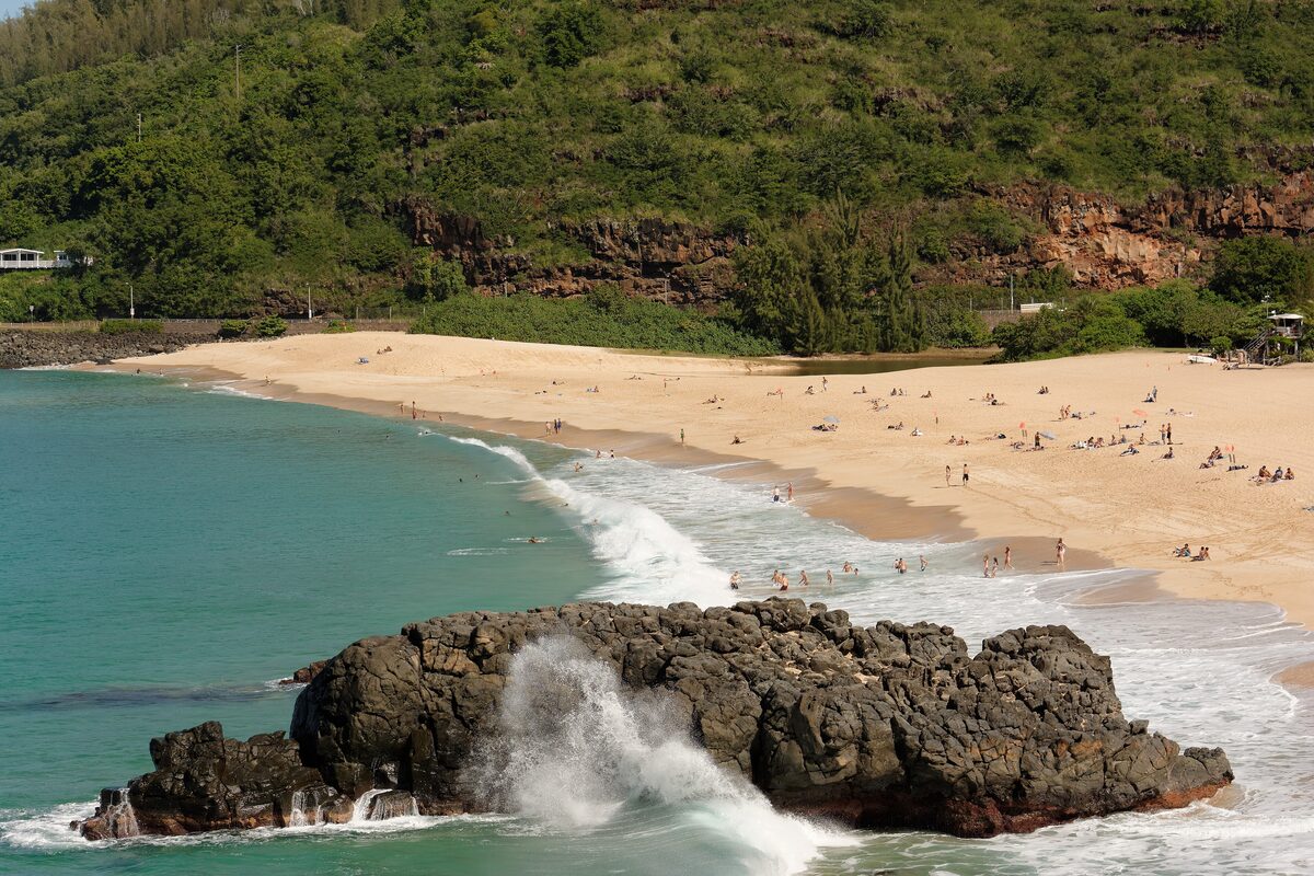 Waimea Bay's golden beach and turquoise water beside a black rock