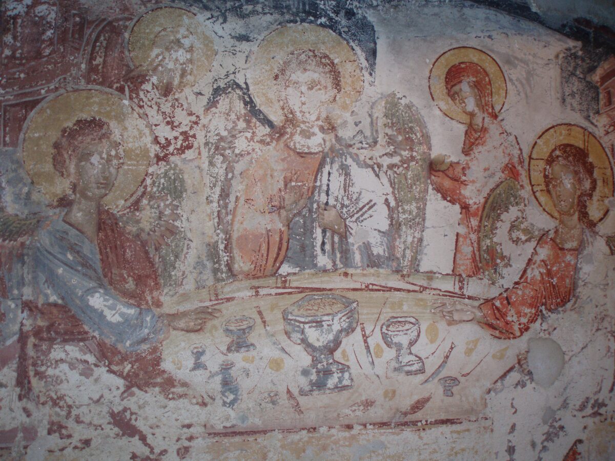 A faded medieval fresco of haloed figures around a table, inside the rock church of the Kališta Monastery