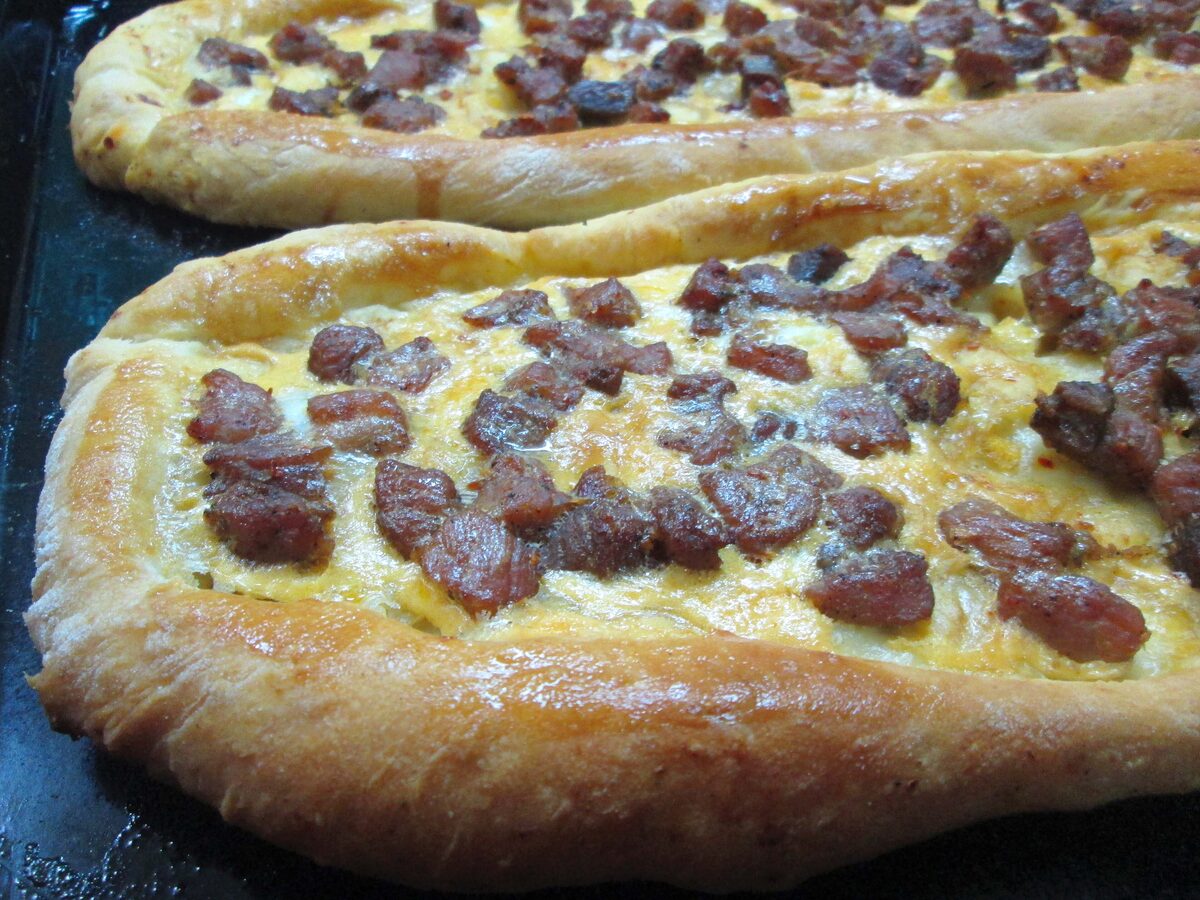 Two boat-shaped pastrmajlija breads topped with browned pieces of meat on a baking tray