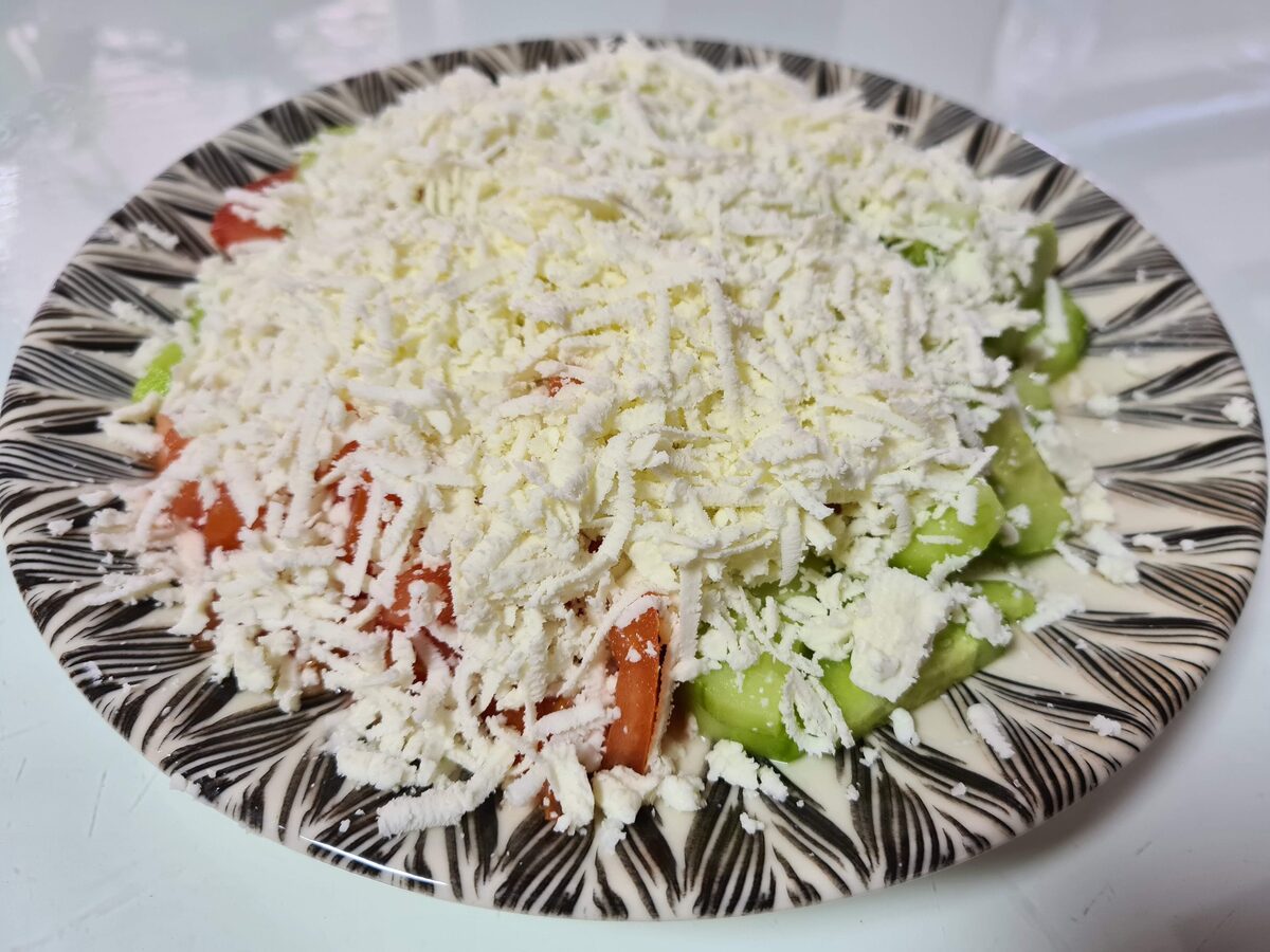 Shopska salad on a patterned plate under a thick layer of grated white sheep cheese