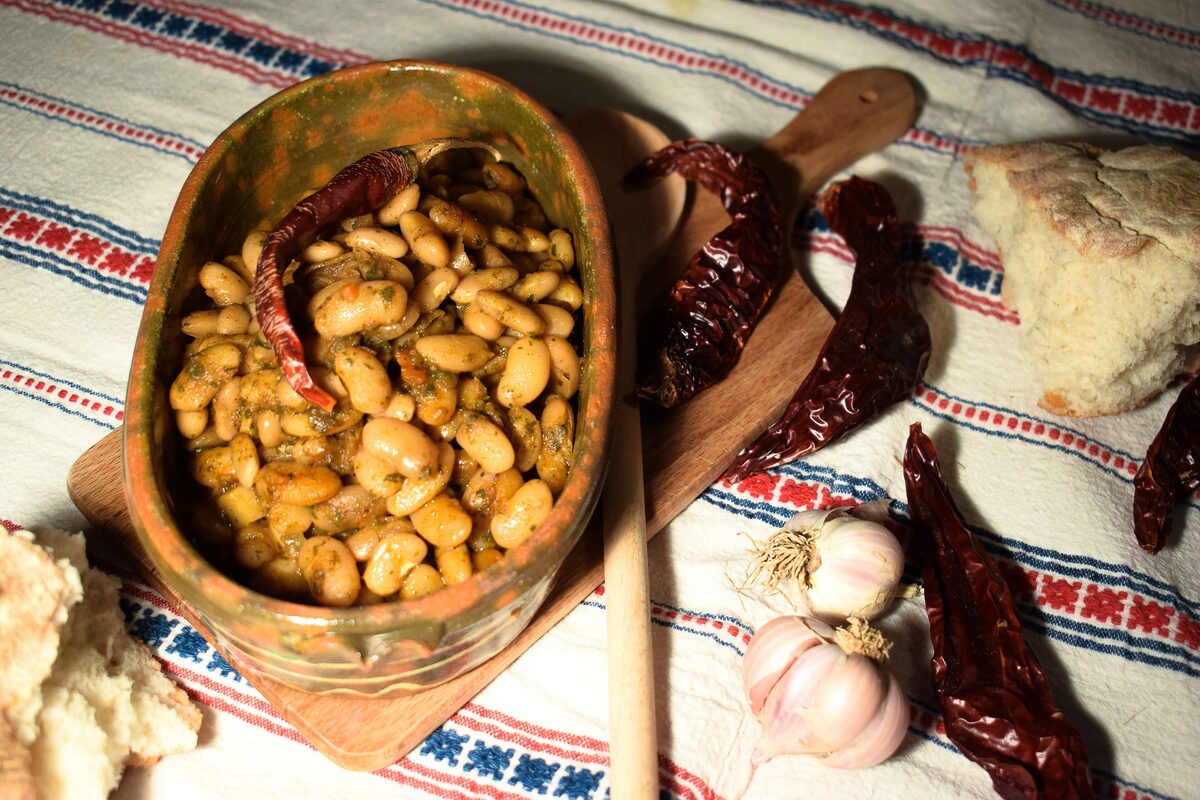 Baked beans in a clay pot with dried peppers and garlic on a woven cloth