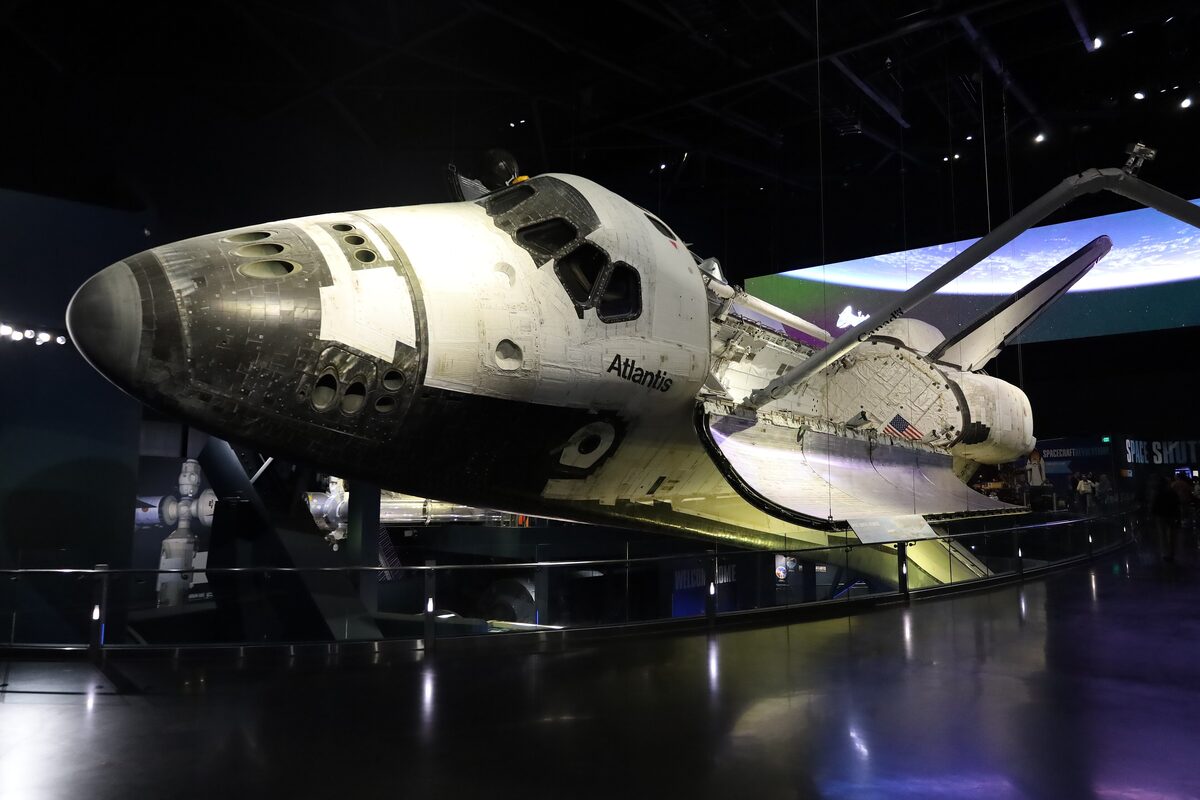 Space Shuttle Atlantis tilted on display with its payload bay doors open inside the dark Atlantis pavilion