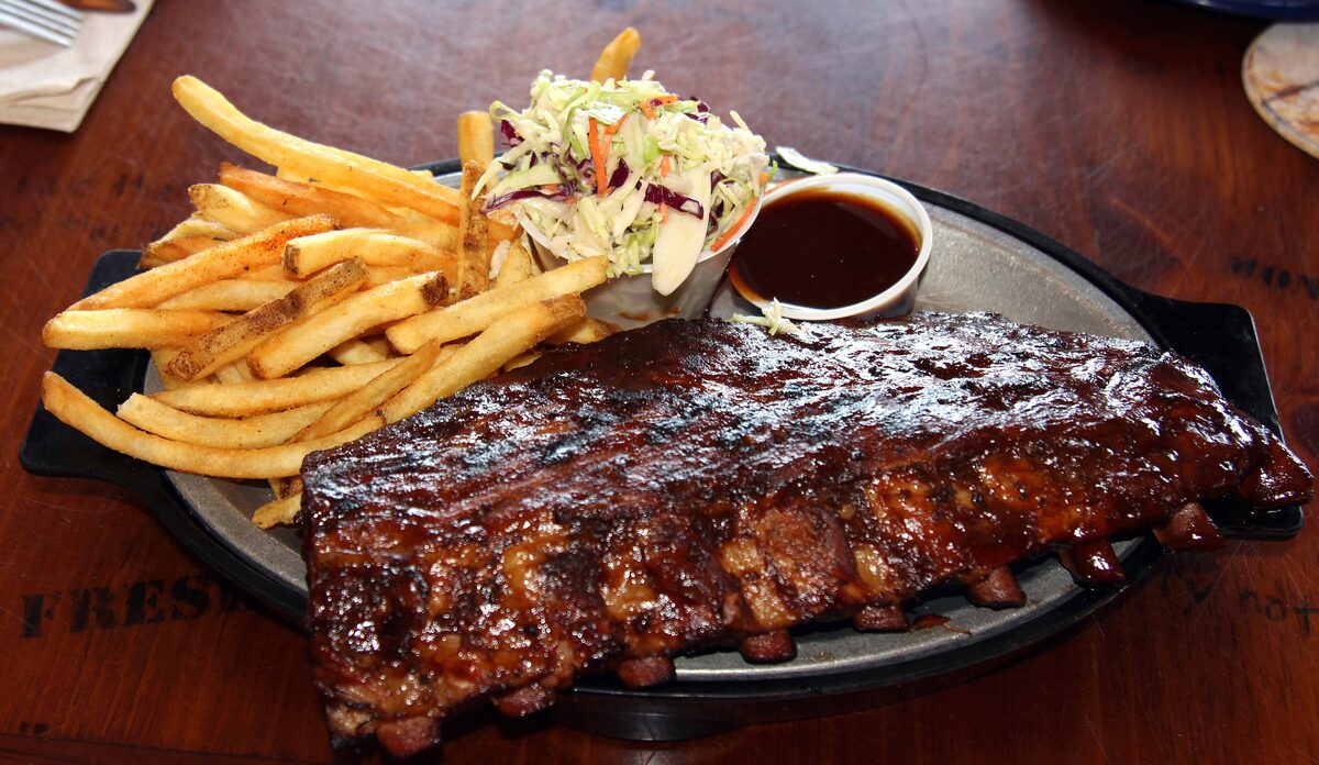 A rack of glazed baby back ribs with fries and coleslaw on a metal platter