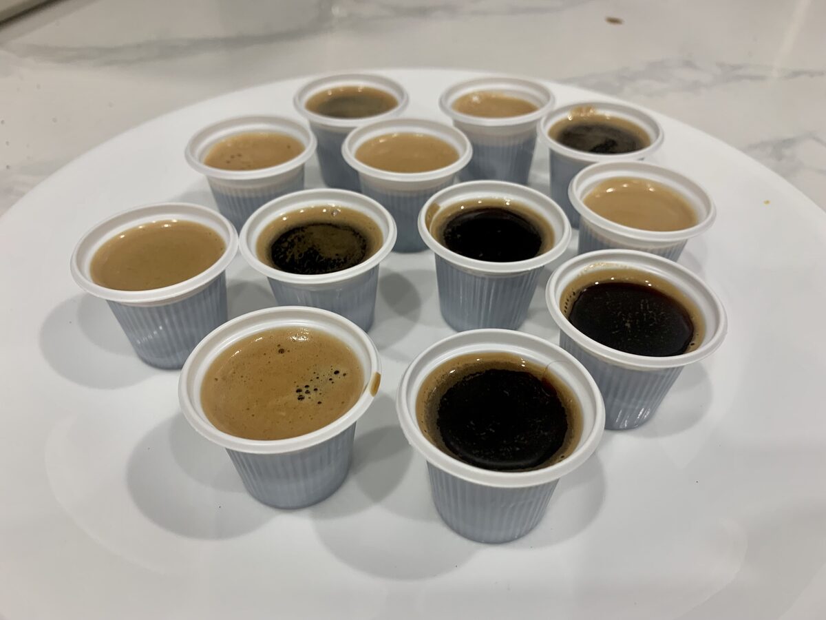A plate of small paper cups filled with Cuban espresso, some dark and some with a creamy foam