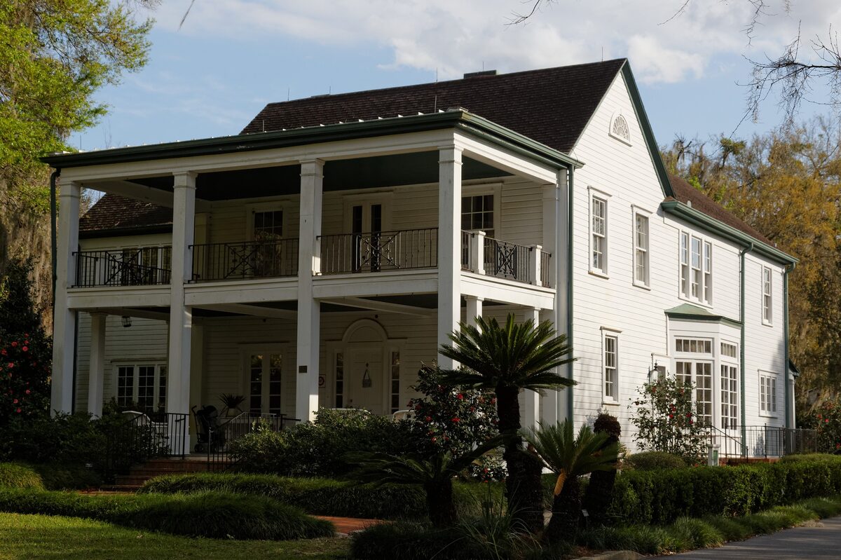 The white two-storey Leu House with a columned veranda, surrounded by palms and lawn in Leu Gardens