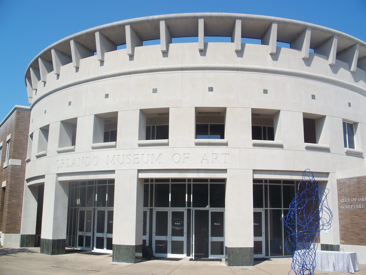 The round, pale concrete drum of the Orlando Museum of Art with its name above the glass entrance and a blue sculpture beside it