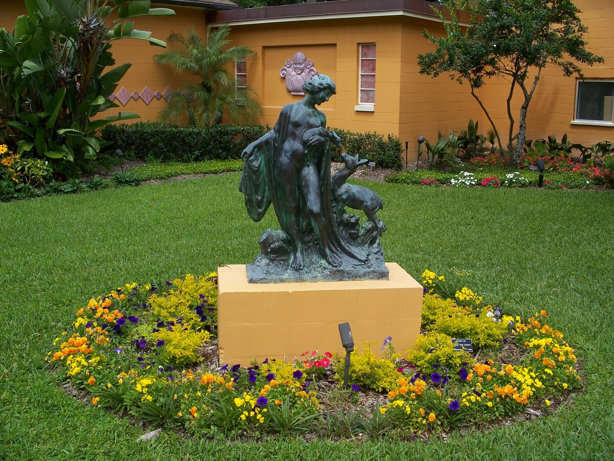 A bronze figure by Albin Polasek on a yellow plinth in a ring of orange and yellow flowers, in the studio garden