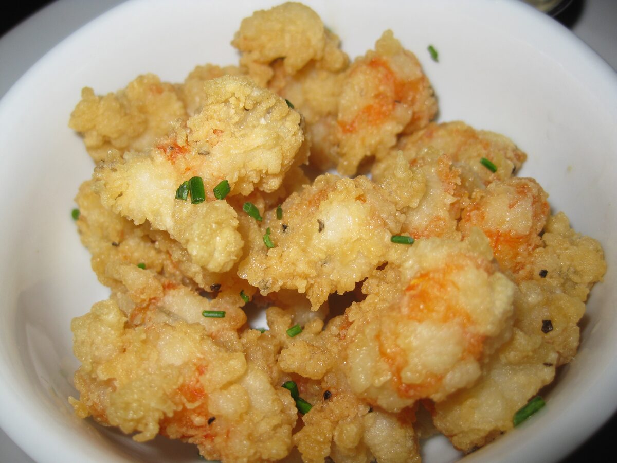 A white bowl of golden fried rock shrimp sprinkled with chives