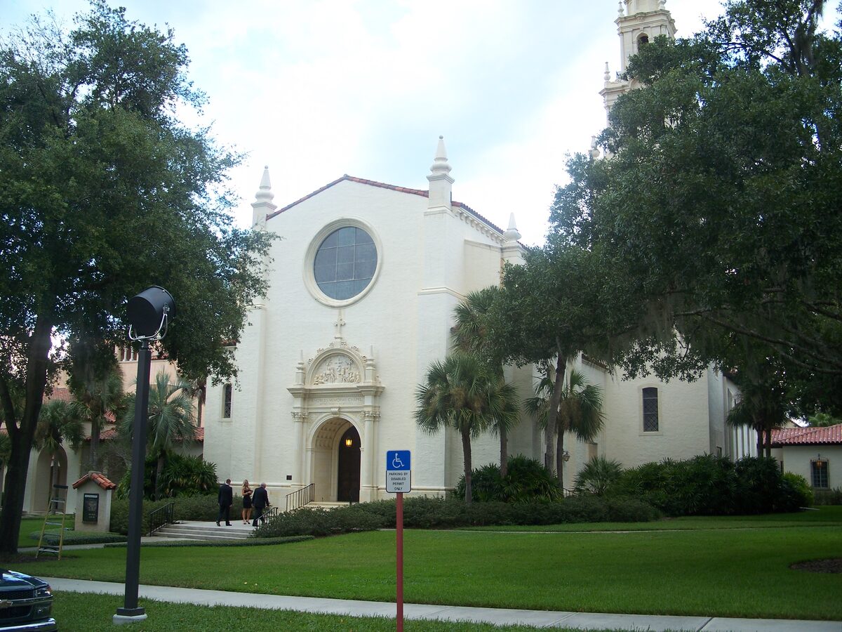 The cream-coloured Knowles Memorial Chapel with its round window and bell tower, across a green lawn on the Rollins College campus