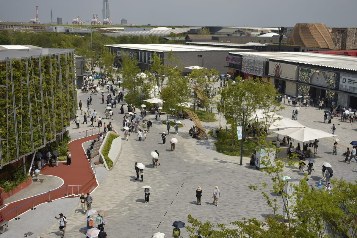 The paved central plaza of the Expo 2025 site on Yumeshima, with trees and visitors walking