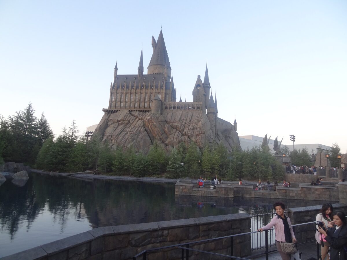 The Hogwarts castle of the Wizarding World of Harry Potter rising over its rock and a still pond, with visitors at the railing