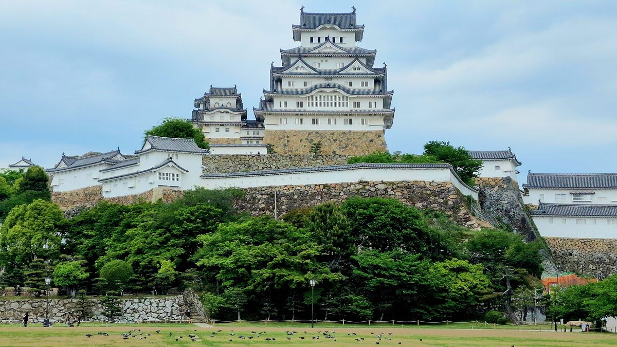 Himeji Castle's white main keep and towers on its stone base, surrounded by green trees