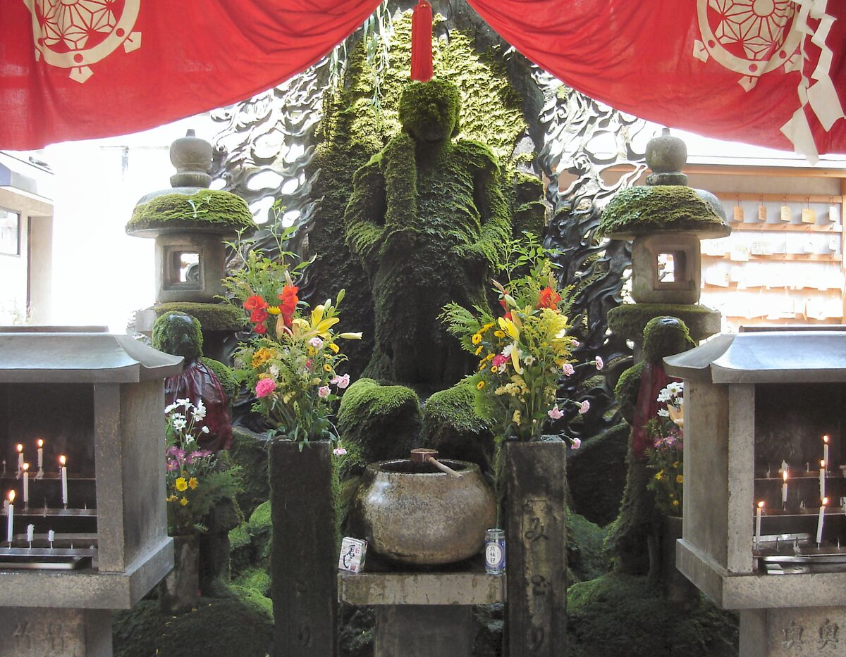 The moss-covered Fudo statue at Hozenji with stone lanterns, candles and a bowl of water in front of it