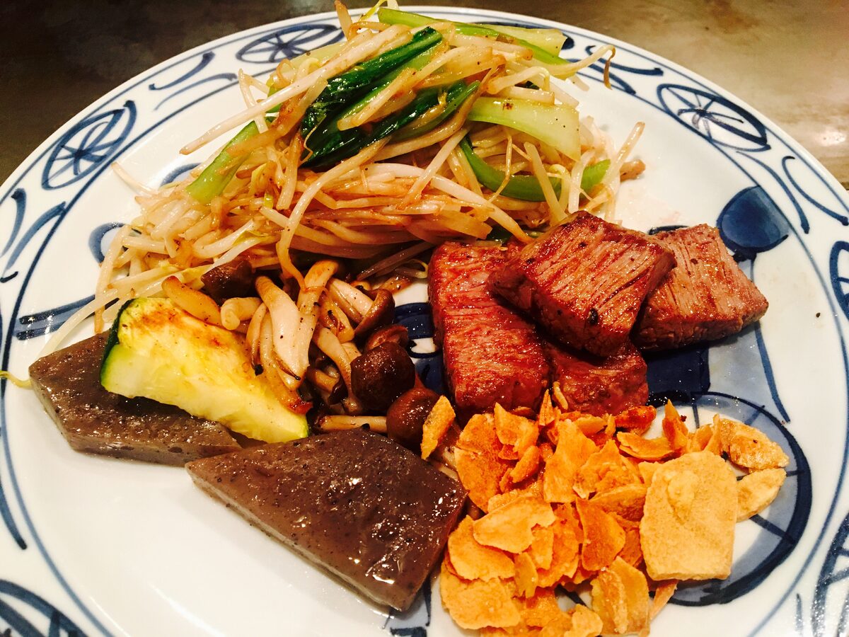A plate of seared Kobe beef cubes with bean sprouts, mushrooms, konjac and garlic chips from a steakhouse in Kobe