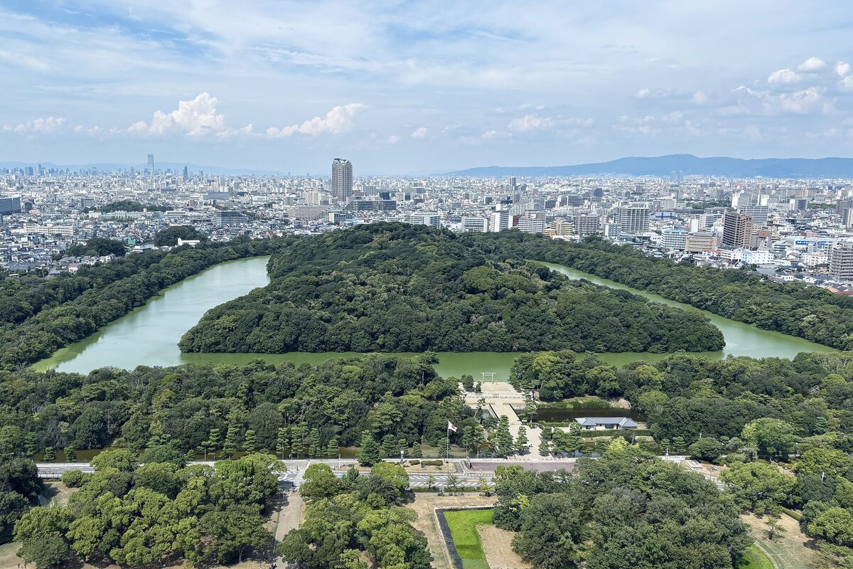 Aerial view of the keyhole-shaped Daisenryo tomb mound, wooded and ringed by a moat, with the Sakai cityscape beyond